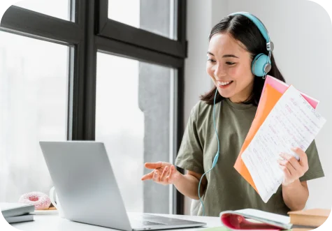 Woman wearing headphones and holding documents beside a laptop
